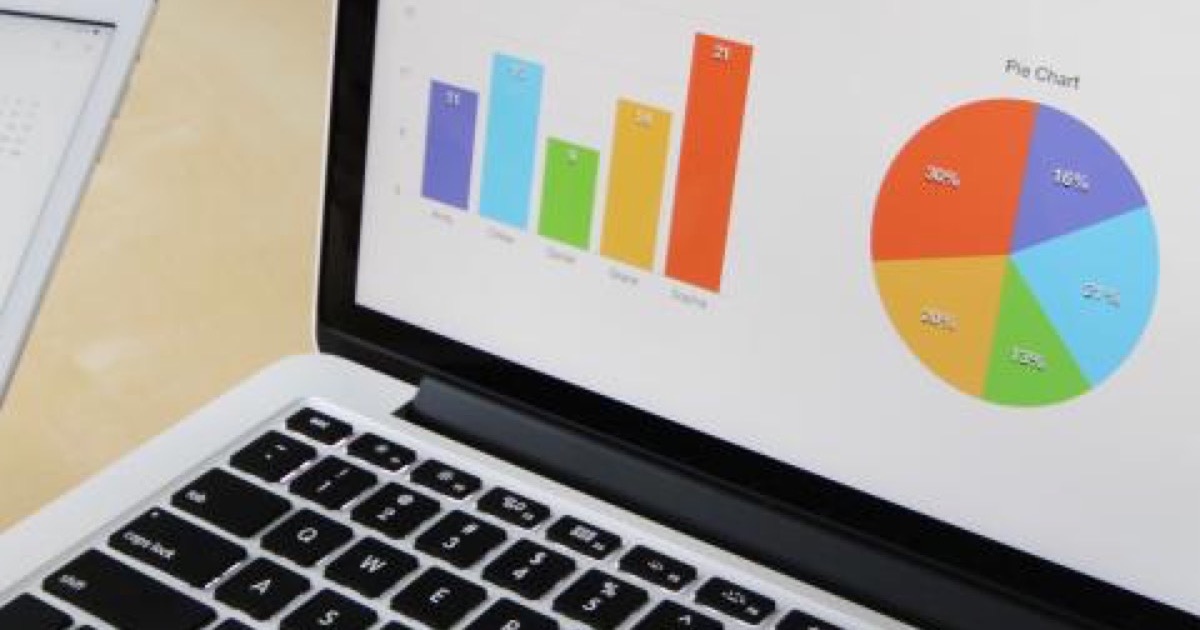 A laptop screen showing a colored bar chart and a pie chart, on a pale wooden desk