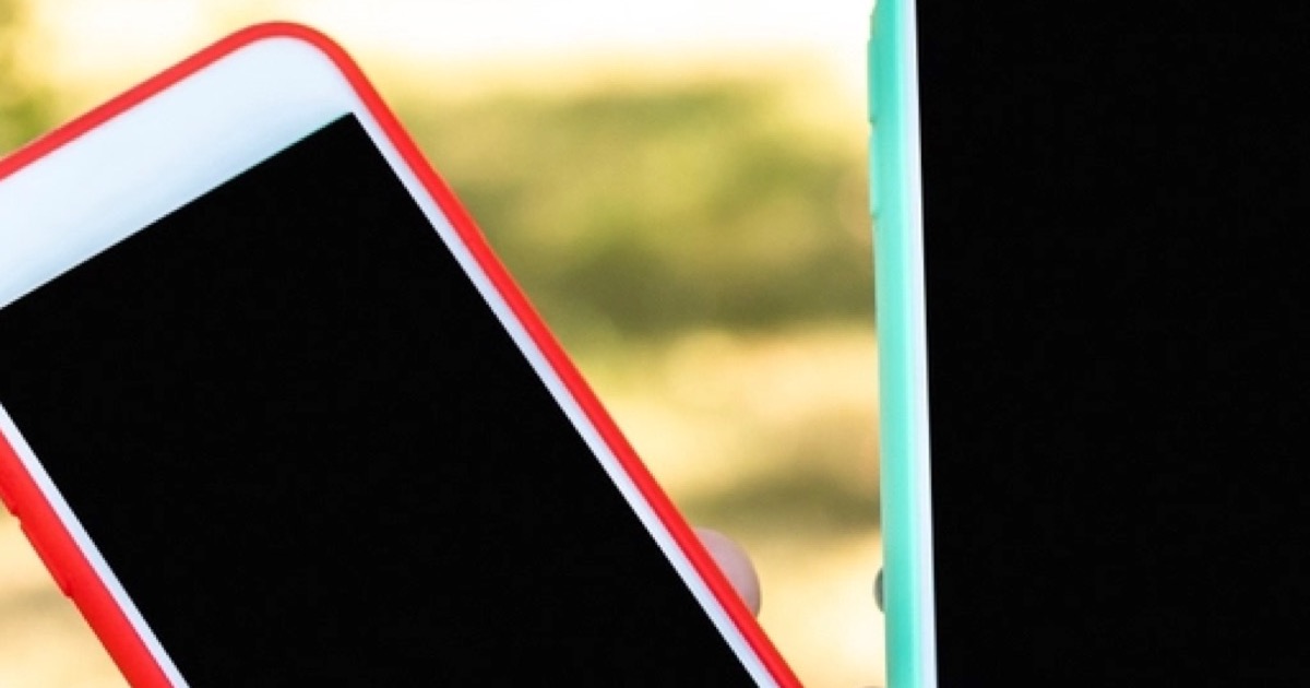 Two phones in red and mint cases held up side by side outdoors, both screens dark
