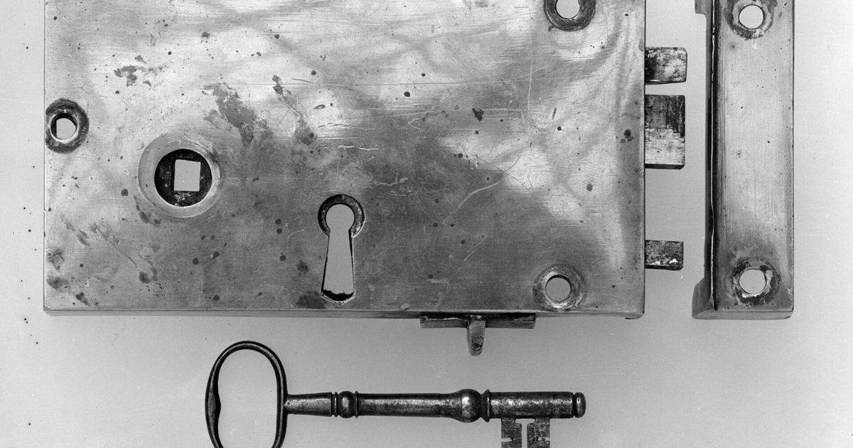 An iron door lock plate with a keyhole, its single key lying below it