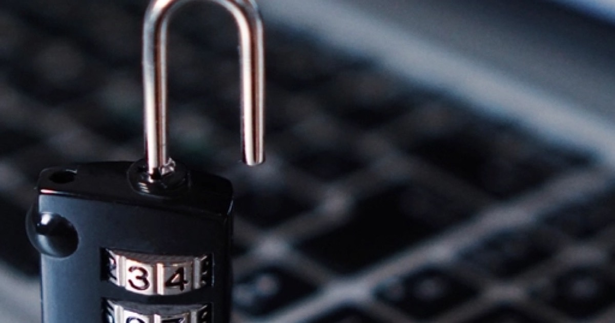 An open combination padlock standing in front of a blurred laptop keyboard