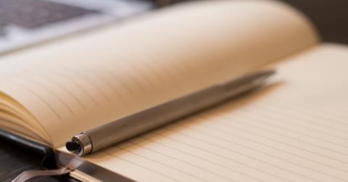 An open lined notebook with a slim silver pen lying in the fold